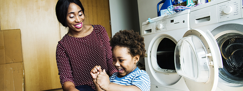Foto av en mamma som leende tittar på sitt barn som leker i en tvättkorg.