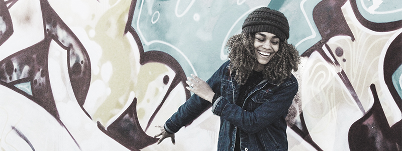 Leende ung kvinna framför en vägg med graffiti