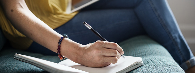En vuxenhand som håller i en penna och antecknar i ett block