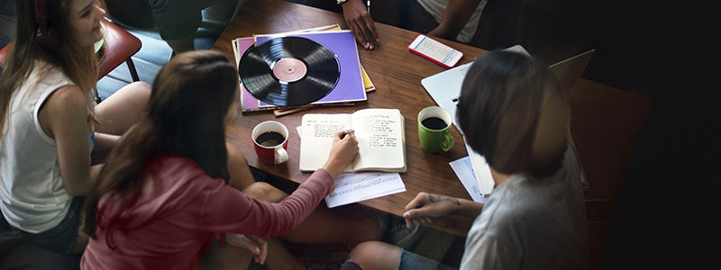 Tonårstjejer runt ett soffbord med kaffemuggar, block och LP-skivor