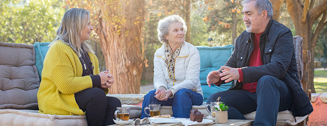 Tre äldre personer sitter utomhus och pratar
