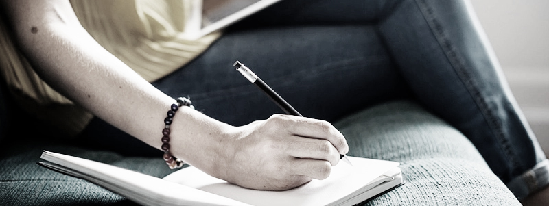 Vuxenhand som håller i en penna och antecknar i ett block